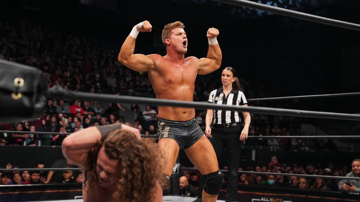 Ryan Nemeth flexing his muscles in an AEW wrestling ring with Jungle Boy on the mat holding his head as a referee looks on