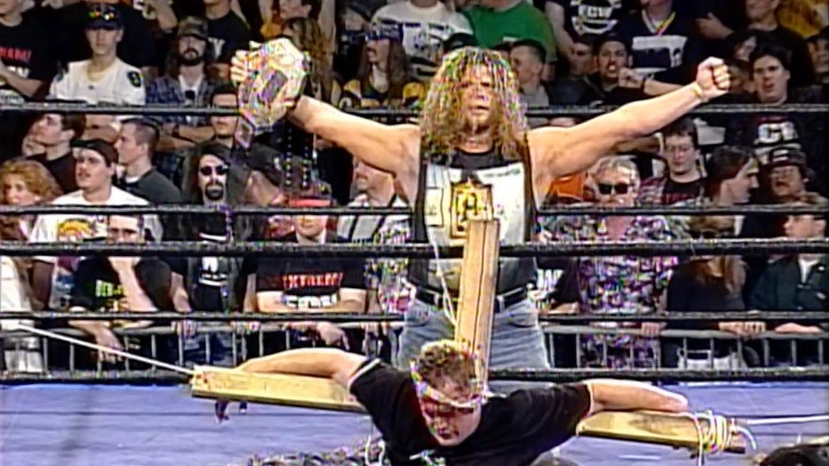 The Sandman strapped to a cross as Raven stands behind him in the ring posing with the ECW World Title