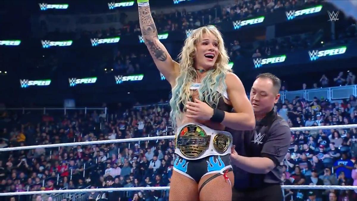 Sol Ruca celebrates inside a wrestlig ring as a referee puts a title belt around Ruca's waist.