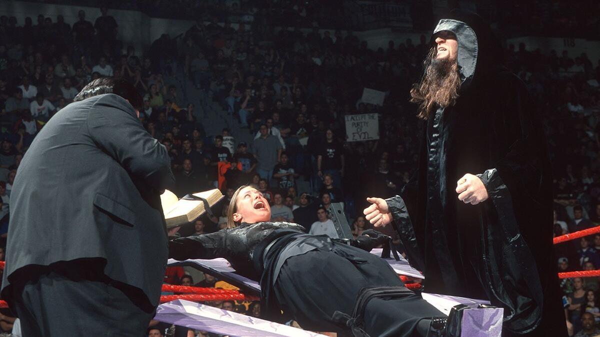 Stephanie McMahon tied to a cross on WWE Raw with the hooded Undertaker looking on 
