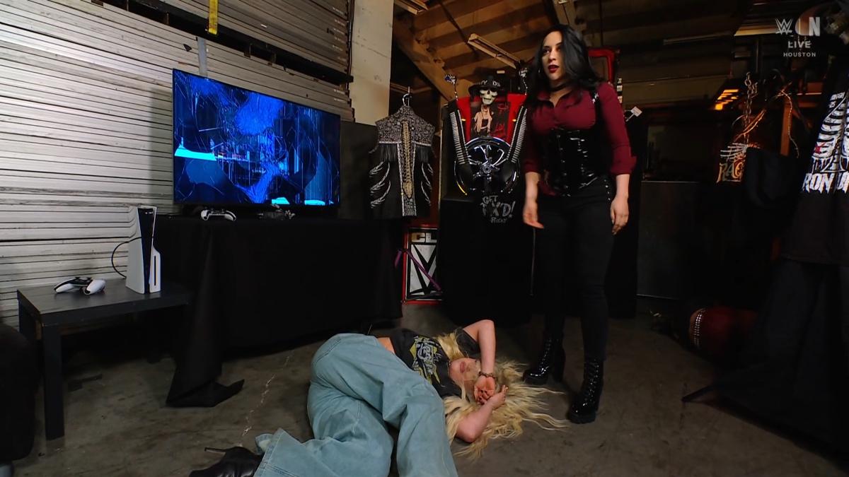 Stephanie Vaquer standing over Liv Morgan, who is lay on the cement as a smashed TV is behind them both