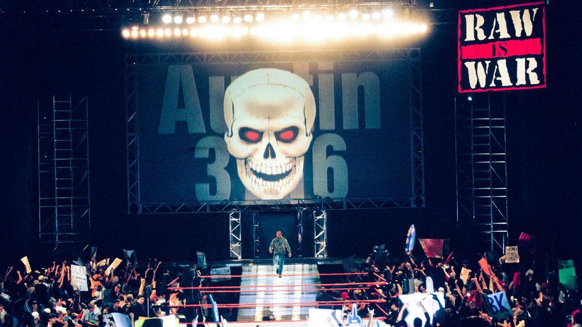 Stone Cold Steve Austin walking down the entrance ramp towards a wrestling ring with an excited crowd cheering him on