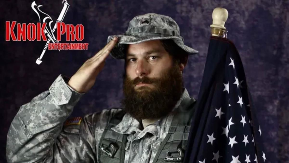 Syko Stu saluting while wearing camouflage and holding the United States flag