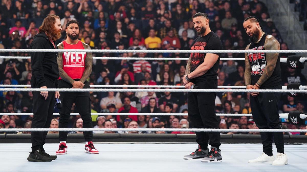 The OG Bloodline stand in a wrestling ring, with a crowd in the background.