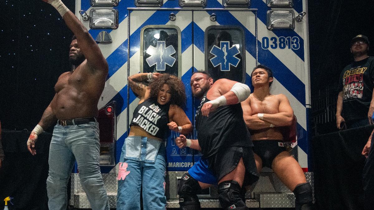 The Opps - Powerhouse Hobbs, Willow Nightingale, Samoa Joe, and Katsuyori Shibata - pose in front of an ambulance in an AEW arena.