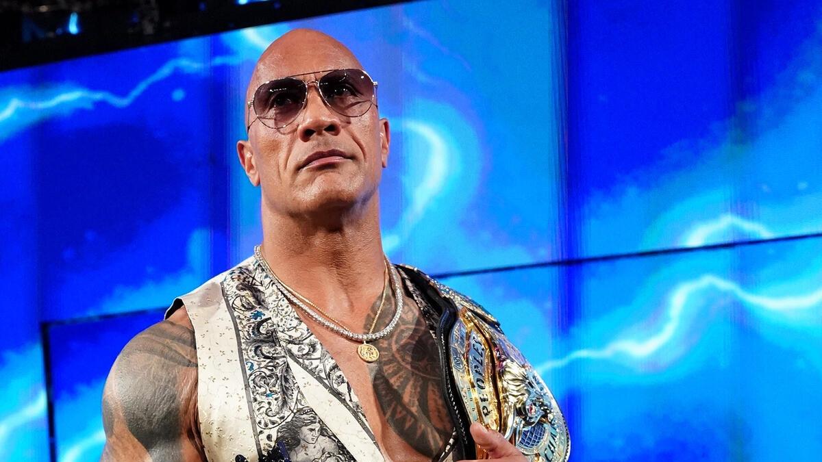 The Rock wearing sunglasses and a paisley vest holding the People's Champion belt on the Bad Blood ram-way