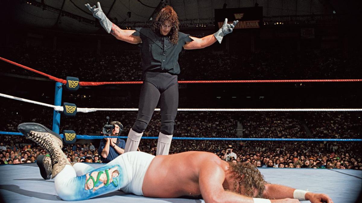 The Undertaker posing in a WWE ring over a downed Jake Roberts