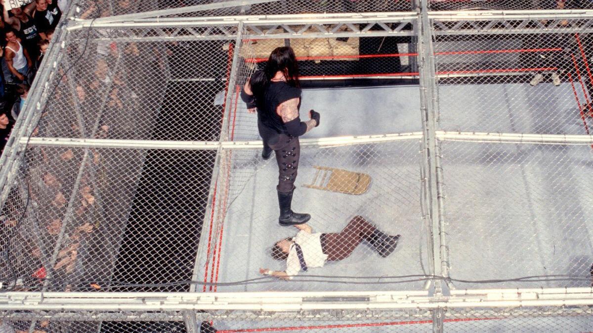 The Undertaker standing on top of Hell in a Cell looking down at Mankind, who is sprawled out on the ring mat 15 ft below. 
