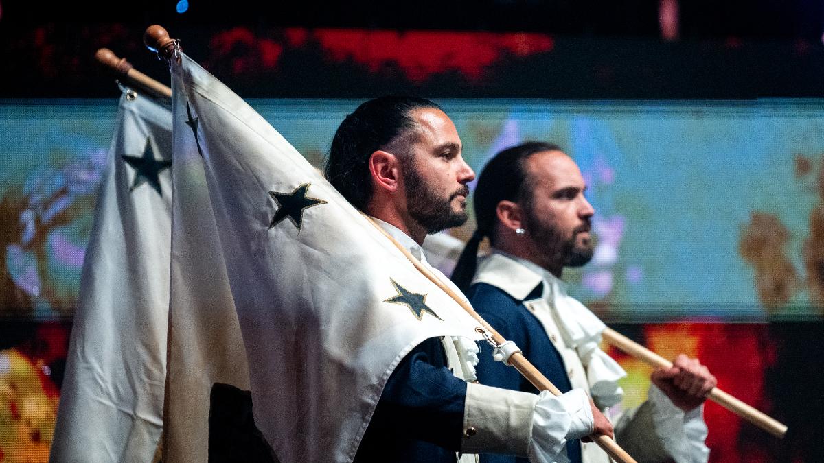 The Young Bucks carrying flags over their shoulders look off camera towards the distance inside an area