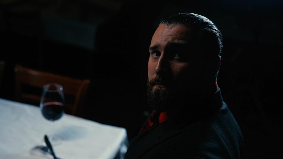 Tony D'Angelo in a suit looking up in the camera as darkness begins to shroud him
