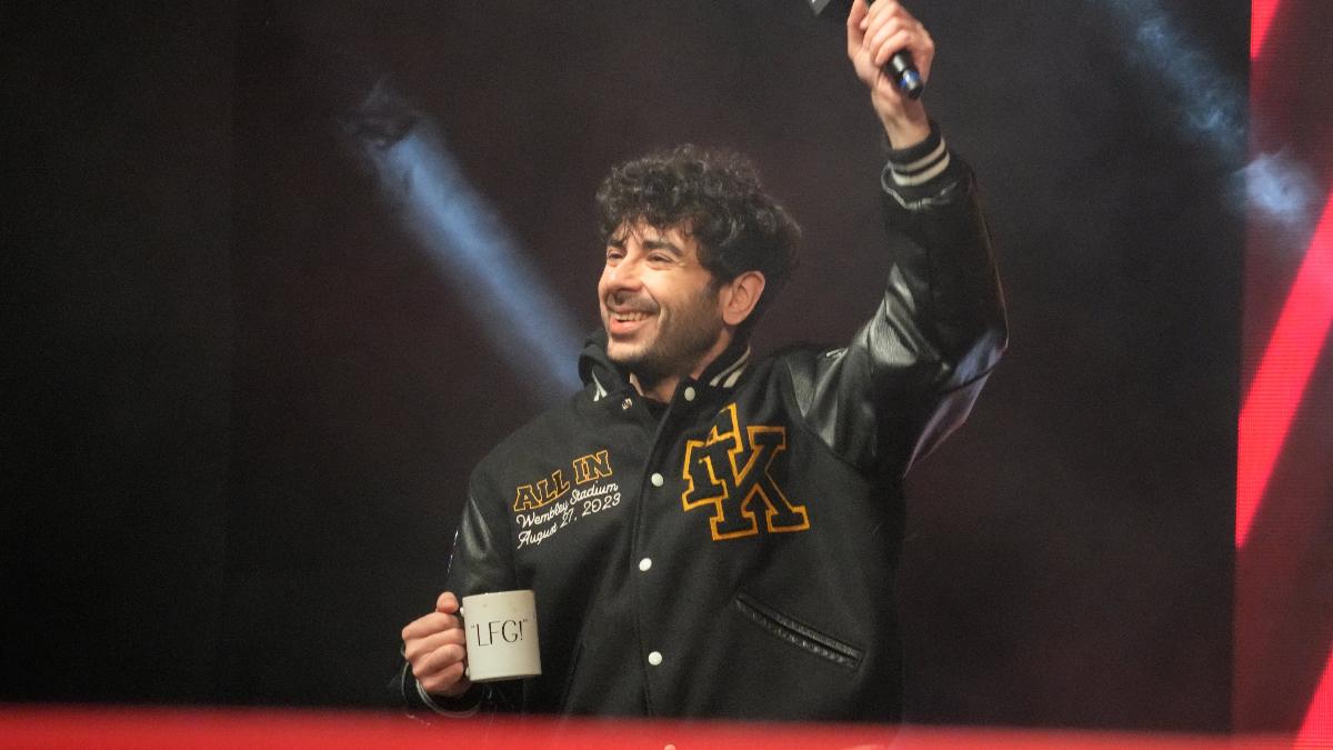 Tony Khan with an 'LFG' coffee cup with his arm raised. Khan also wears a varsity jacket with his initials 'TK' on