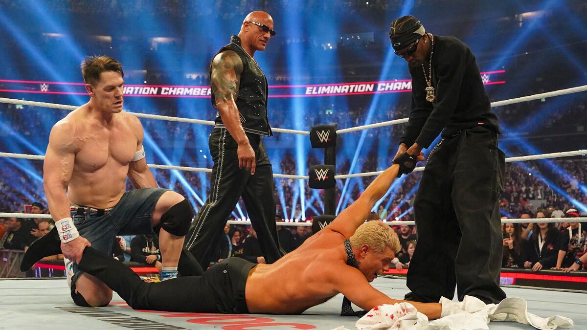 Travis Scott dragging Cody Rhodes while John Cena holds Rhodes down at WWE Elimination Chamber