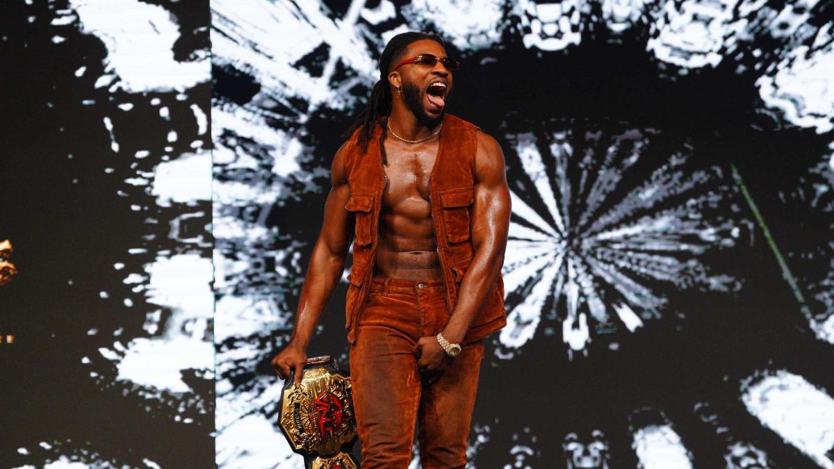 Trick Williams in sunglasses and waistcoat walking to the ring holding the TNA World Championship