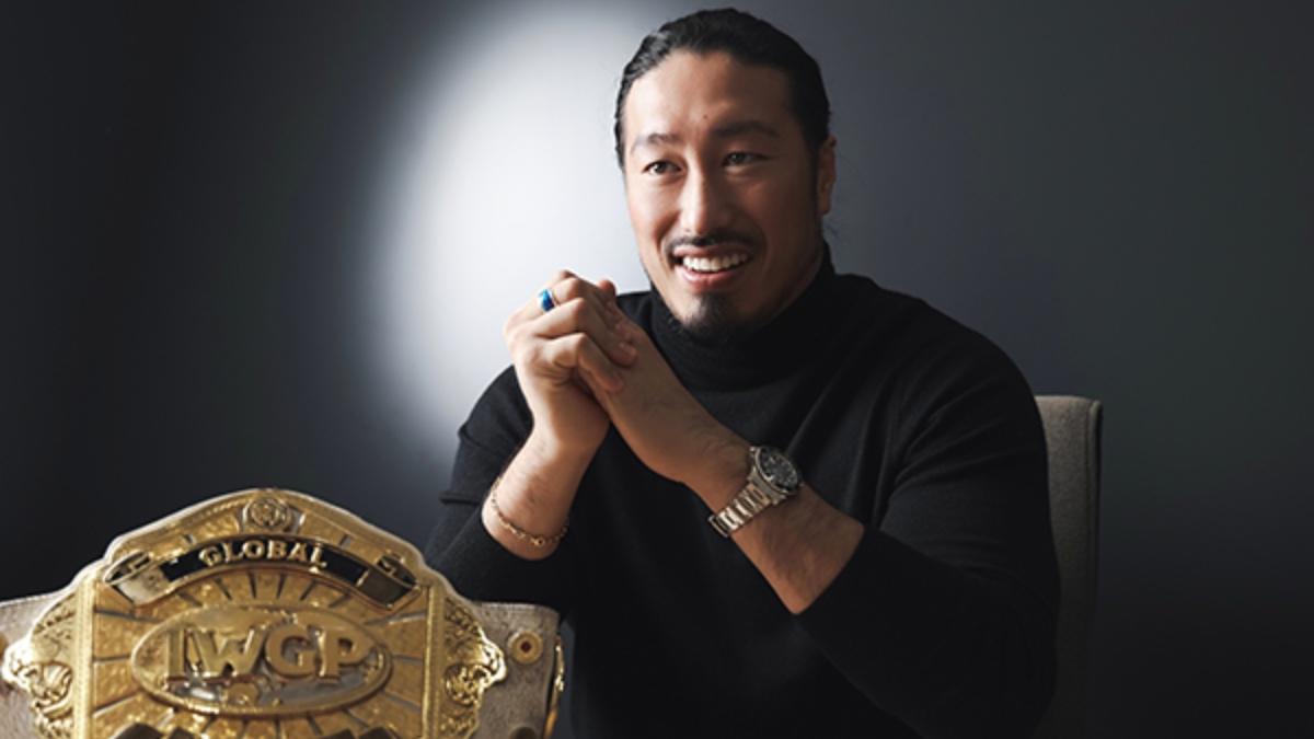 Yota Tsuji wearing a black turtleneck swear sitting at a desk with the IWGP Global Heavyweight Title