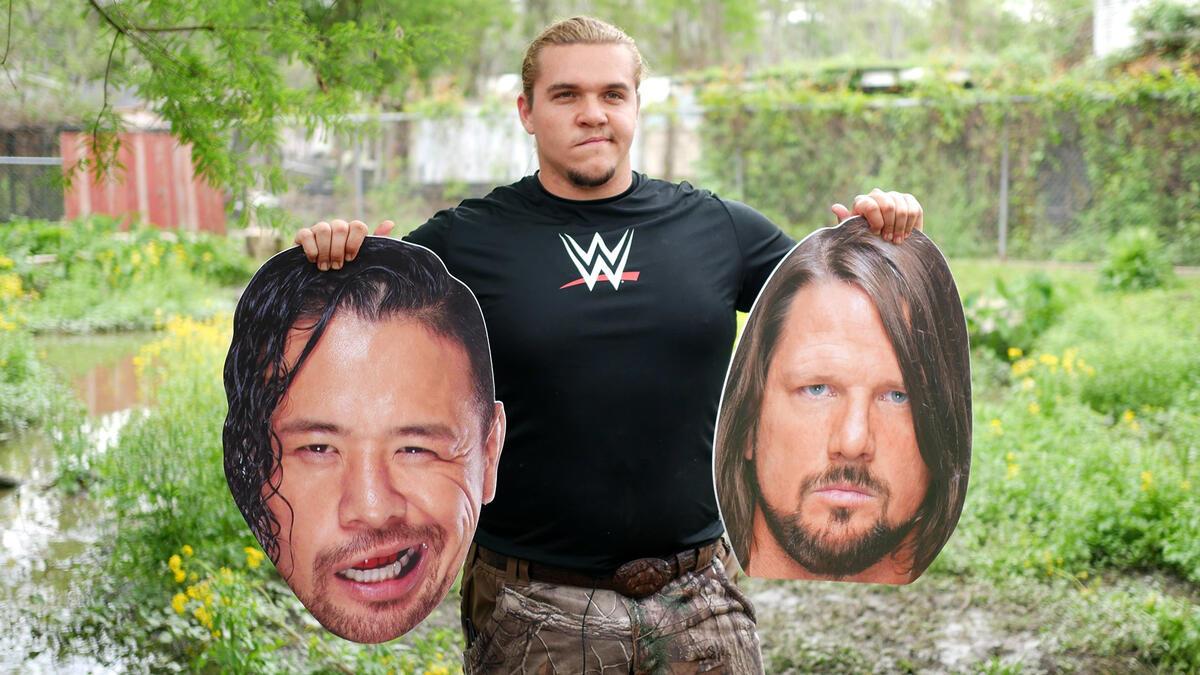 2015 WWE Tough Enough contestant ZZ holds giant cardboard cutout heads of AJ Styles and Shinsuke Nakamura