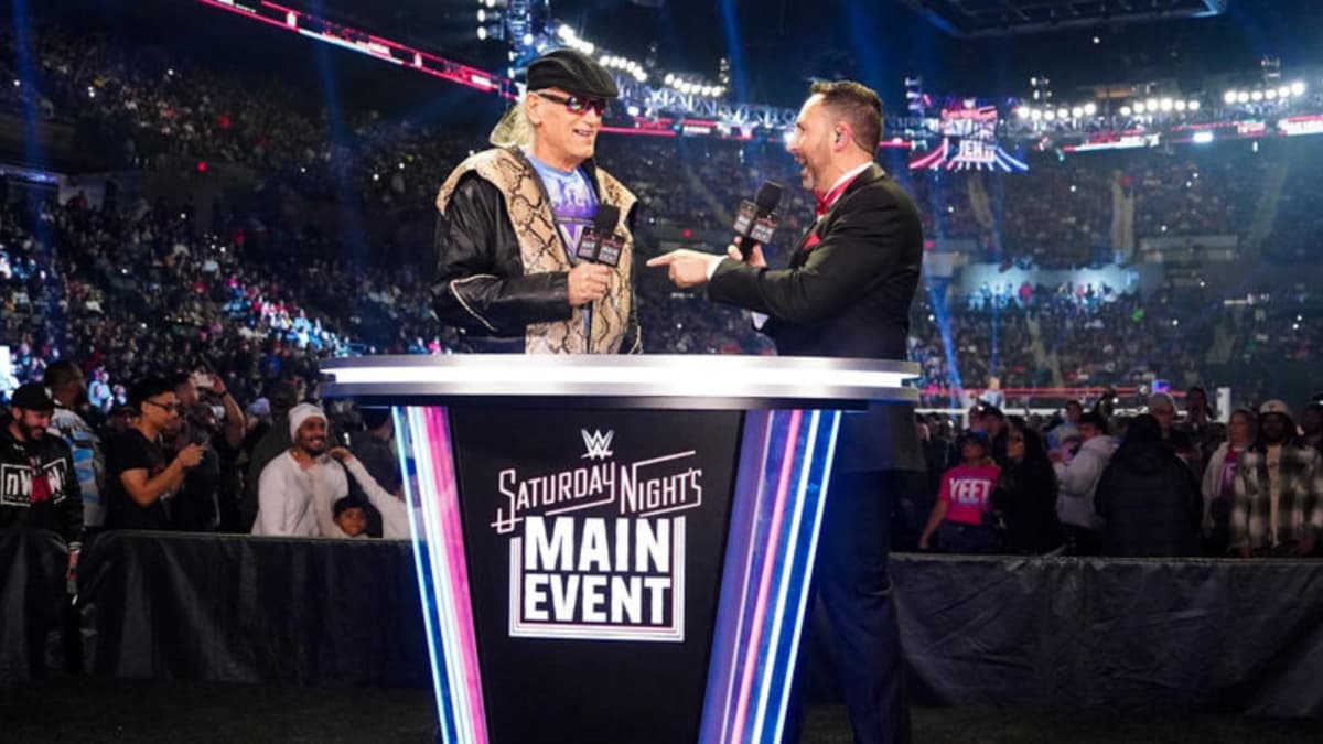 Jesse Ventura and Joe Tessitore talking by a Saturday Night's Main Event podium