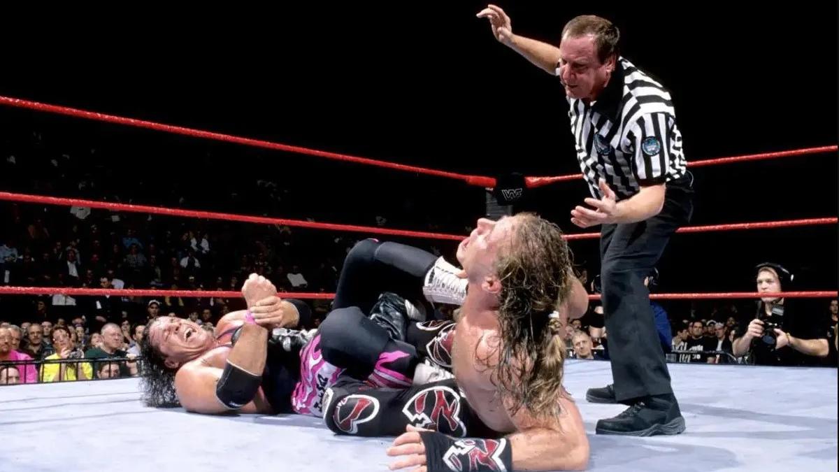 Bret Hart with Shawn Michaels in a Figure Four Leglock as referee Earl Hebner stands above them