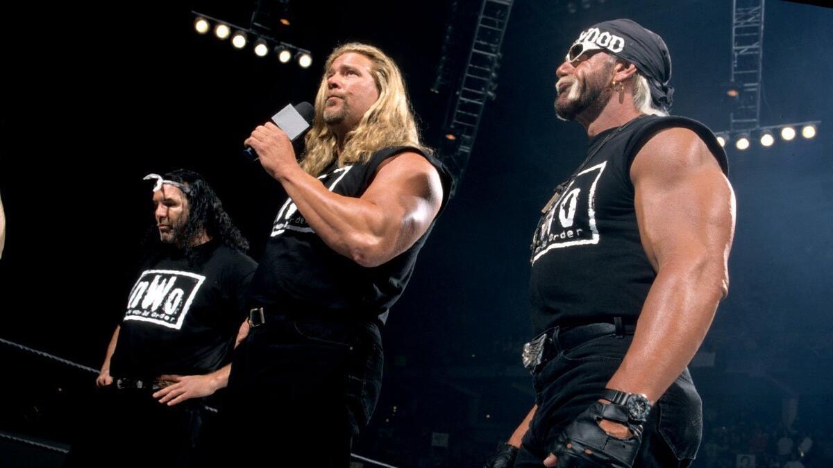 Hollywood Hogan to the right, Kevin Nash in the middle with a microphone, and Scott Hall on the left with a bandana on his head all wearing NWO t-shirts at WWE No Way Out 2002