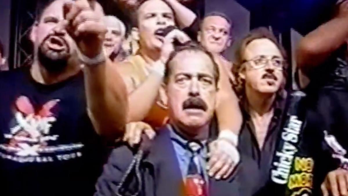 Jimmy Hart and other wrestlers standing on a stage shouting